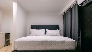 Un lit avec une tête de lit sombre, une literie blanche et une petite table de chevet avec une lampe.