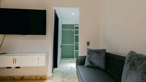 A living room with a black sofa, a flat-screen TV mounted on the wall, and a white radiator below. - Habitacion Deluxe cama extragrande A-204 (Punta Cana)
