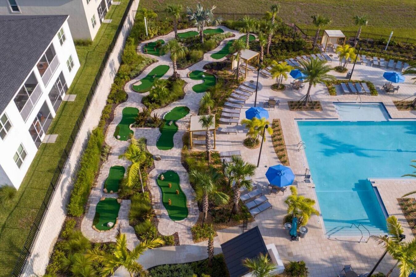 En vy från ovan över en golfbana med ett poolområde, inklusive en swimmingpool, solstolar och palmer.