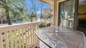 Un balcon avec vue sur un lac et des arbres, une table en métal et une porte-fenêtre coulissante.