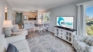 Ein modernes Wohnzimmer mit Flachbildfernseher, weißen Sofas, einem Essbereich mit Bar und Blick ins Freie.