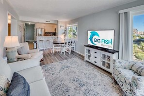 Ein modernes Wohnzimmer mit Flachbildfernseher, weißen Sofas, einem Essbereich mit Bar und Blick ins Freie.