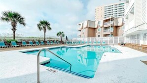 Ein Swimmingpool mit Liegestühlen und Palmen, umgeben von einem Gebäude mit Balkonen.