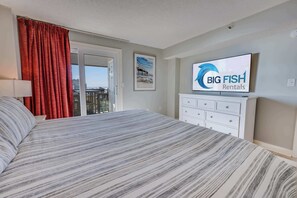 Habitación de hotel con una cama grande, un televisor montado en la pared, una ventana con cortinas rojas y vista a la ciudad.