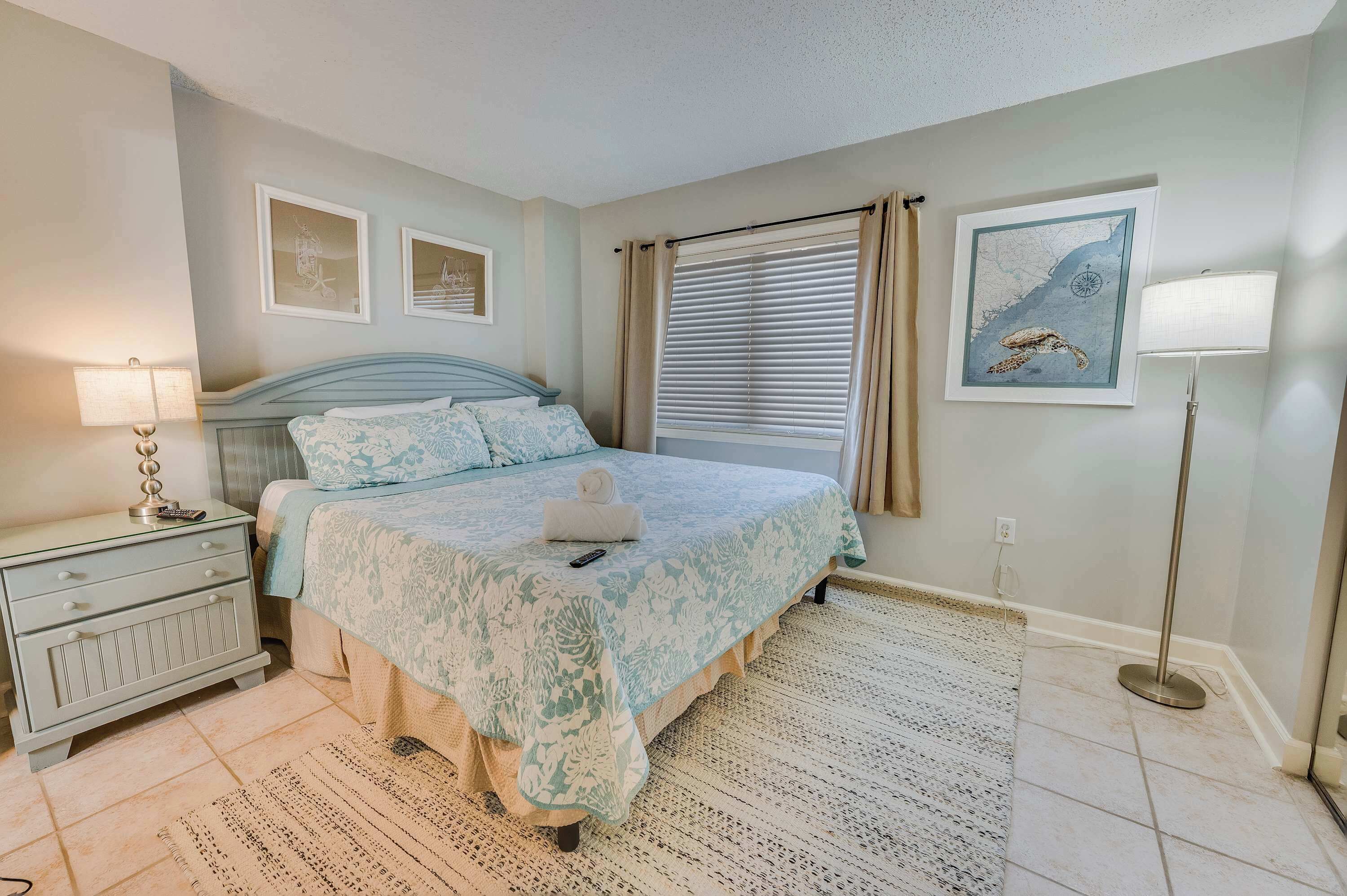 A bedroom with a bed, bedside table, lamp, and artwork on the wall.