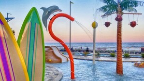 Un parc aquatique avec une sculpture de dauphin, un palmier et des planches de surf colorées.