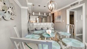 Uma área de refeições moderna com uma mesa de vidro redonda, cadeiras brancas e um lustre.