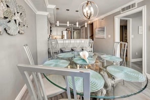 A modern dining area with a round glass table, white chairs, and a chandelier. - Luxury 2 Story Oceanfront Penthouse at the  Palms (Myrtle Beach)