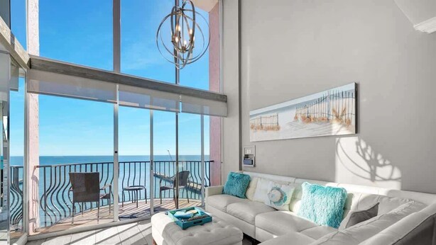 Varanda espaçosa com vista para o mar, um sofá branco com almofadas verde-água e um lustre moderno.