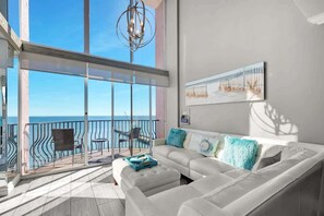 A spacious balcony with a view of the sea, a white sofa with teal cushions, and a modern chandelier. - Luxury 2 Story Oceanfront Penthouse at the  Palms (Myrtle Beach)