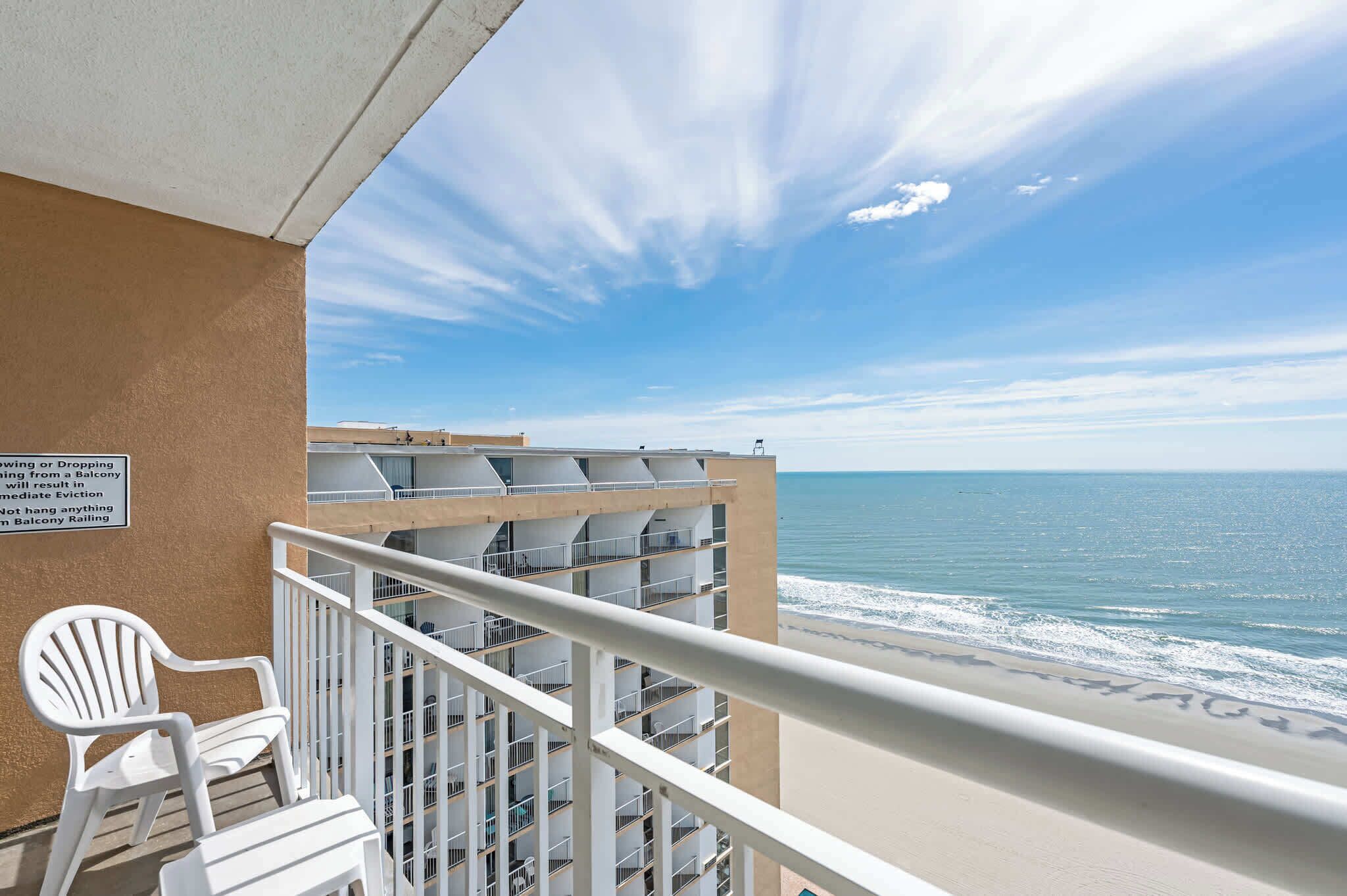 A balcony with a white chair, a view of the ocean, and a building with multiple balconies.