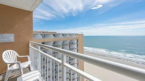 Ein Balkon mit weißem Stuhl, Blick auf das Meer und ein Gebäude mit mehreren Balkonen.