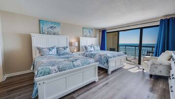 Un dormitorio con dos camas, un balcón con vista al océano y una silla blanca.