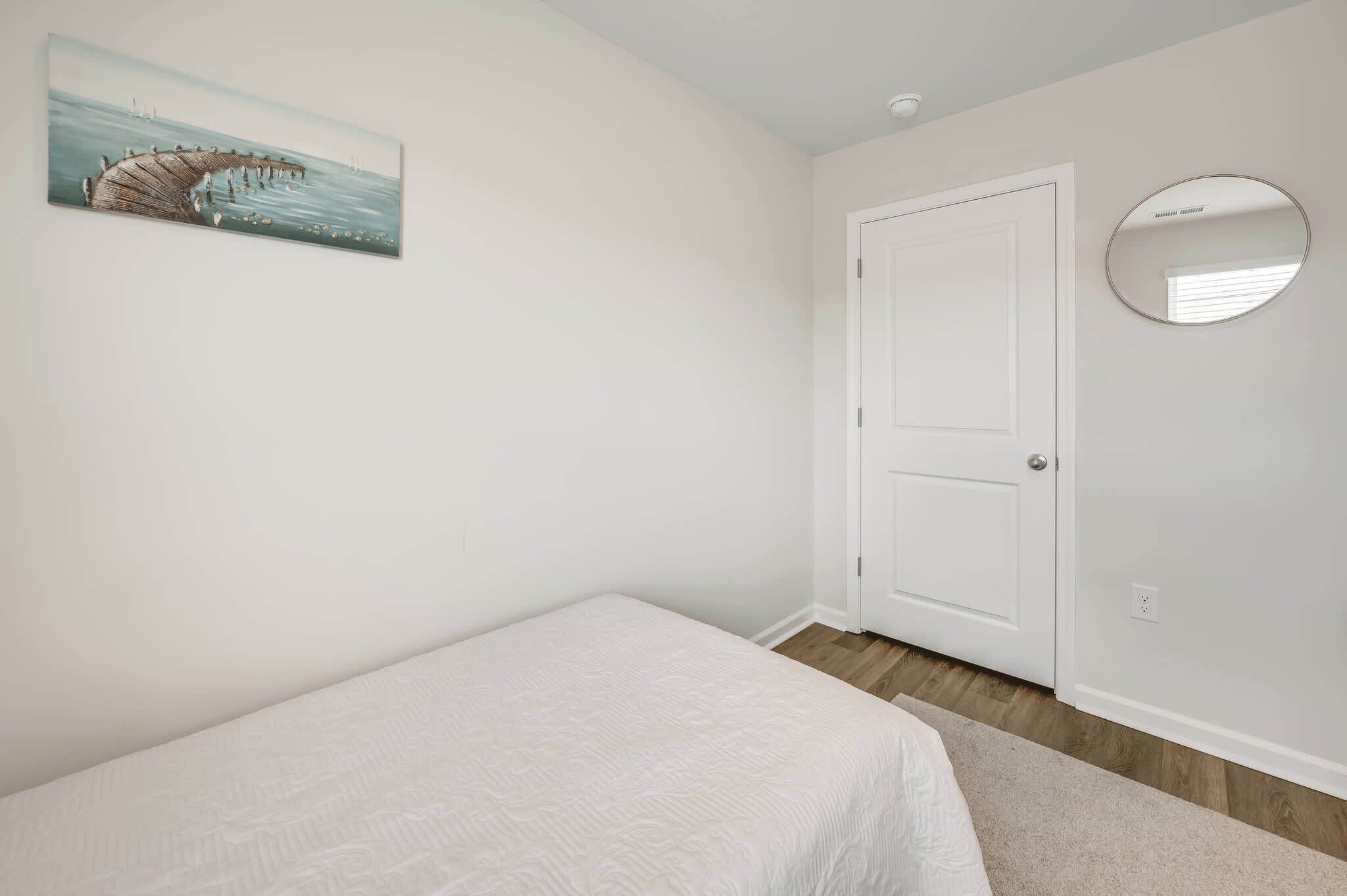 A bedroom with a bed, a door, a wall-mounted mirror, and a painting.