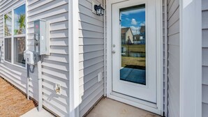 Une maison blanche avec une porte d’entrée, une fenêtre et un coffret électrique.