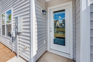 A white house with a front door, a window, and an electrical box.