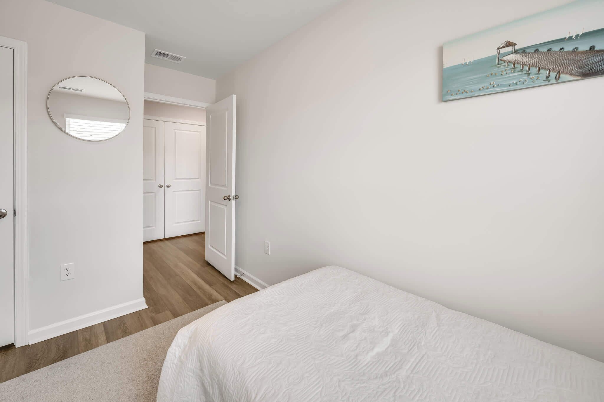 A bedroom with a bed, a round mirror, a door, and a painting on the wall.