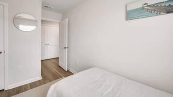 A bedroom with a bed, a round mirror, a door, and a painting on the wall.
