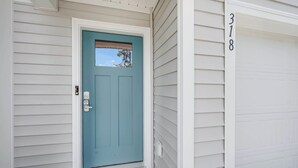 Une maison avec une porte d’entrée de couleur turquoise, un revêtement extérieur blanc et une porte de garage portant le numéro 318.