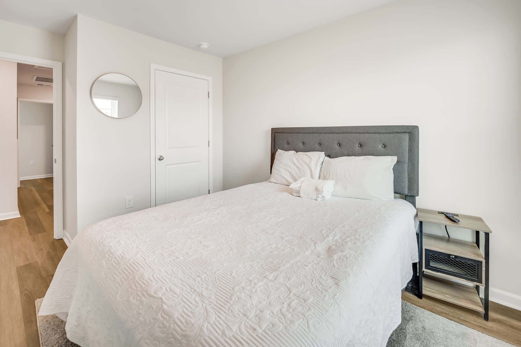 Un dormitorio con cama, mesita de noche, espejo y puerta.
