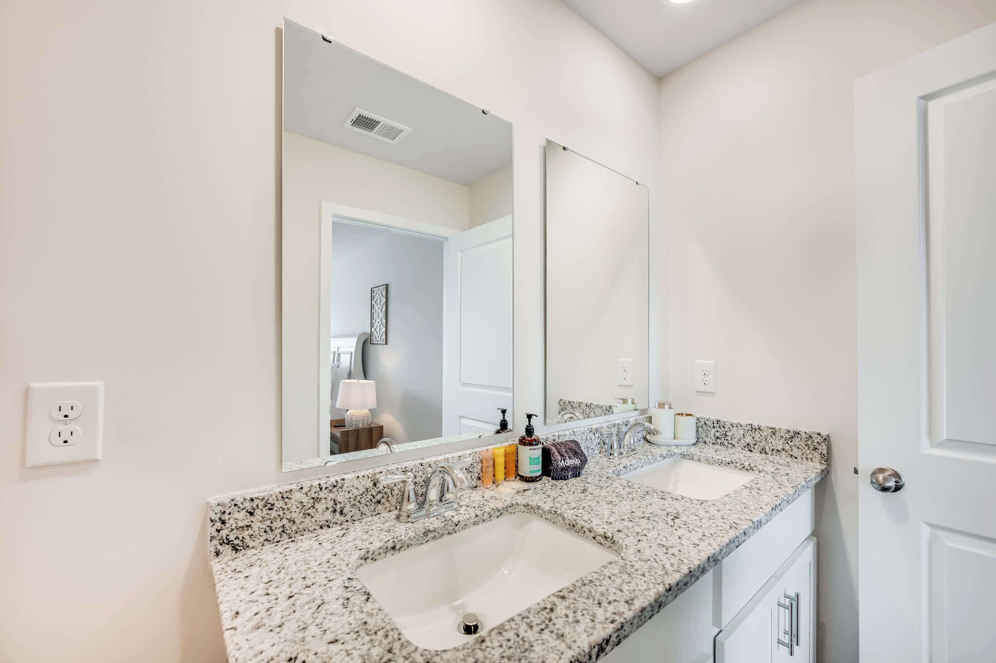 Une salle de bain avec deux lavabos, un grand miroir et une porte.