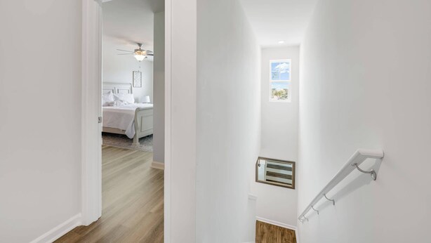 Un couloir avec un lit en arrière-plan, un ventilateur de plafond et un radiateur fixé au mur.