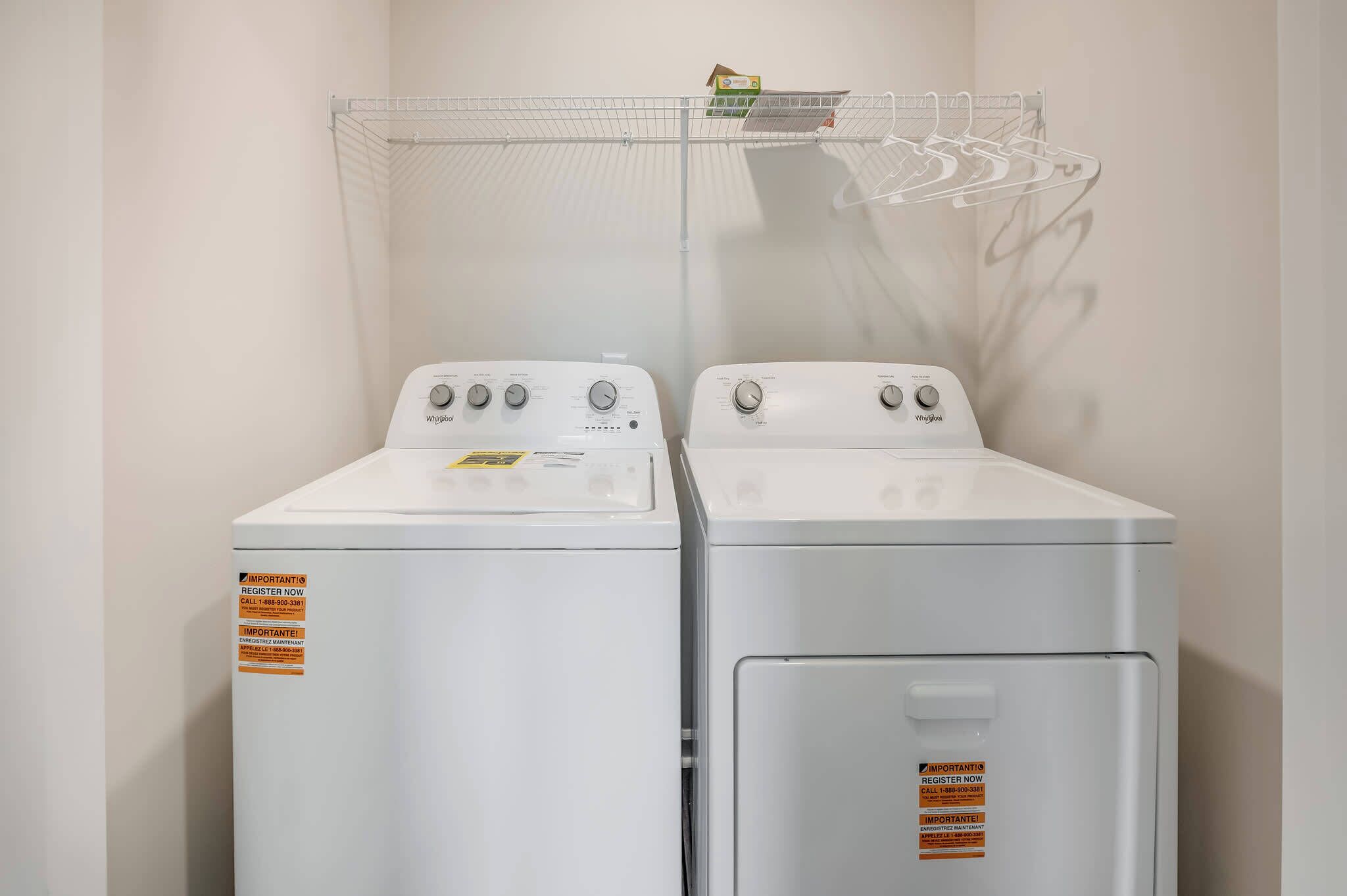 Deux lave-linge à chargement frontal blancs, dotés de boutons de commande, et un étendoir métallique placé au-dessus.