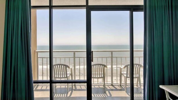 A room with a large sliding glass door leading to a balcony with beach chairs and a view of the ocean. - Direct Oceanfront 1BR, Pools at Sands Ocean Annies (Myrtle Beach)