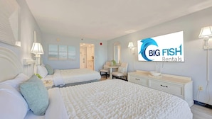 Ett hotellrum med en stor säng, ett skrivbord och en stol. På väggen hänger en tv och det finns en skylt med texten ”BIG FISH Rentals”.