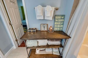 Une salle de bain avec un meuble-lavabo en bois, des serviettes, un panneau indiquant « SURF, SABLON, SOLEIL, BAIGNADE », et une photo encadrée posée sur le comptoir.