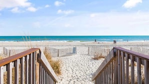 A wooden boardwalk leading to a sandy beach with a clear blue sky.