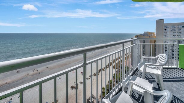A balcony with a view of a beach and ocean, white plastic chairs, and a green awning. - Amazing Penthouse at Coral Beach with Heated Pools (Myrtle Beach)
