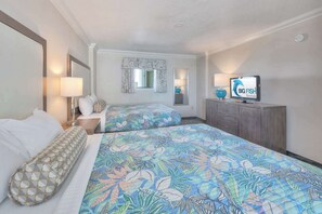 Ein Hotelzimmer mit zwei Betten, einem Fernseher, einem Schreibtisch und einem Fenster mit Vorhängen.