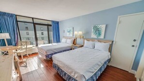Una camera d'albergo con due letti, una scrivania, una sedia e un'ampia finestra con tende.