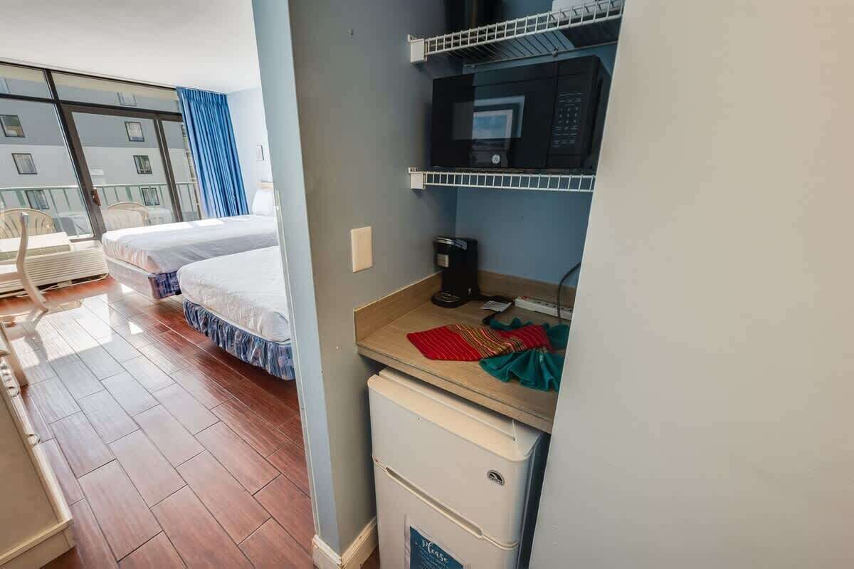 Een hotelkamer met twee bedden, een kitchenette, een magnetron en een kleine koelkast.