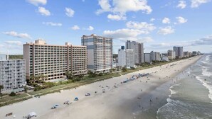 Un hôtel situé en bord de mer, composé de plusieurs immeubles de grande hauteur, avec une plage de sable et une vue sur l’océan.