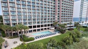 Un hôtel de grande hauteur doté de nombreux balcons, d’une piscine et d’un jardin bien entretenu.