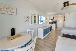 Ein Zimmer mit Esstisch, Bett, Deckenventilator, Fernseher und Küchenzeile.