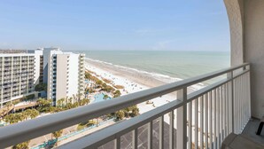 Un balcone con vista su una spiaggia, una piscina e l'edificio di un hotel.