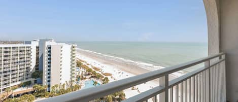 A balcony with a view of a beach, a pool, and a hotel building.
