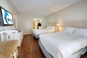 Une chambre d’hôtel avec deux lits, un bureau, une chaise et un téléviseur diffusant des publicités pour « BIG FISH Rentals ».