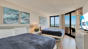 Quarto de hotel com duas camas, obras de arte nas paredes, televisão e vista para o mar.