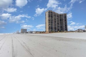 A beachfront hotel with a curved facade, a sandy beach in the foreground, and a clear sky. - 2BR Remodeled Oceanview in Private Maisons Sur Mer (Myrtle Beach)