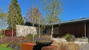 A modern building with a stone facade, a wooden fence, and a well-maintained garden with various plants and a large planter. - The One - Kinloch (Kinloch)