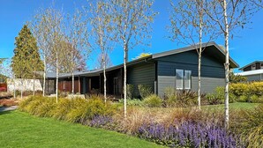 A modern house with a covered porch, a stone wall, and a well-maintained garden with purple flowers. - The One - Kinloch (Kinloch)
