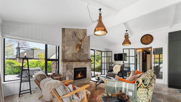A spacious living room with a fireplace, seating area, and large windows offering a view of greenery. - The One - Kinloch (Kinloch)