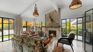 A spacious living room with a fireplace, large windows, and a deer head mounted on the wall. - The One - Kinloch (Kinloch)