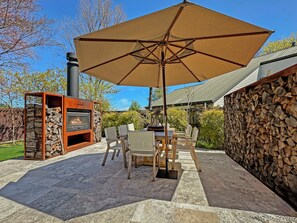 Une terrasse extérieure avec une cheminée en pierre, une table avec des chaises et un grand parasol.