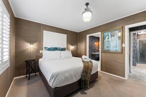 Une chambre à coucher comprenant un lit, une table de chevet, une lampe fixée au mur et un grand tableau encadré.