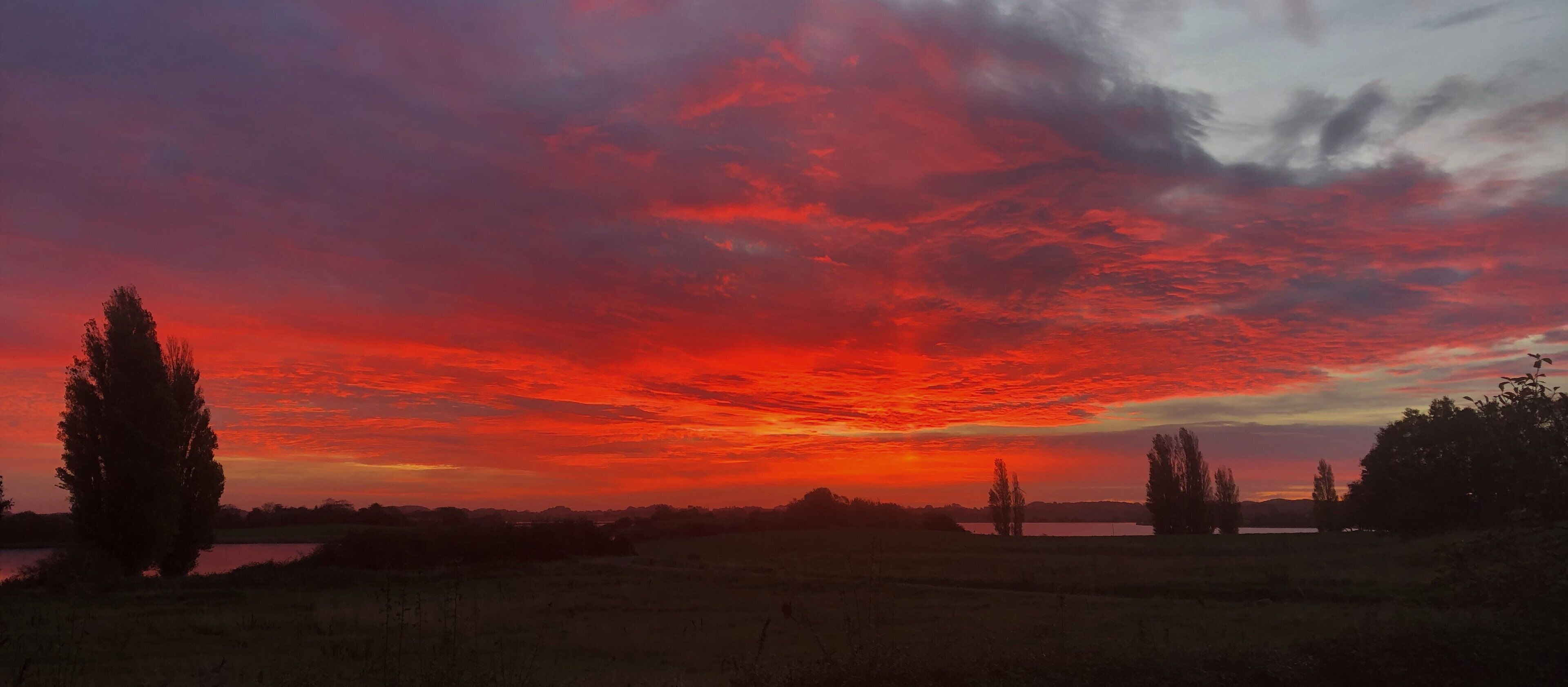 Ein Sonnenuntergang über einer ländlichen Landschaft mit Bäumen und Feldern.